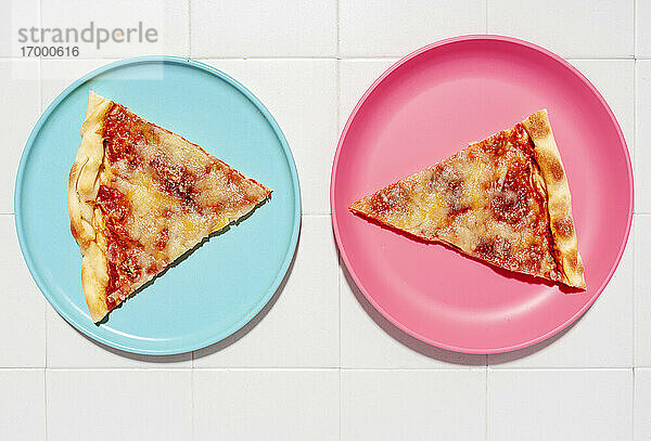 Zwei Scheiben Pizza Margherita auf blauen und rosa Tellern