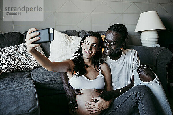 Lächelnde schwangere Frau macht Selfie mit jungem Mann zu Hause