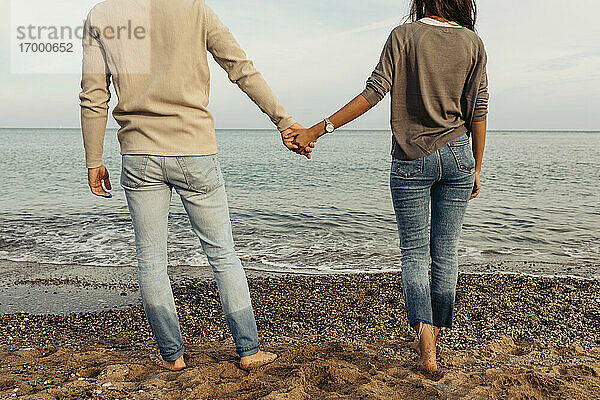 Junges Paar hält sich an den Händen  während es am Strand im Sand steht