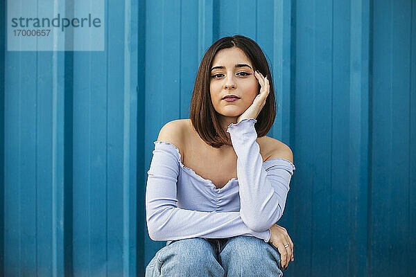 Junge schöne Frau sitzt gegen blaue Wand