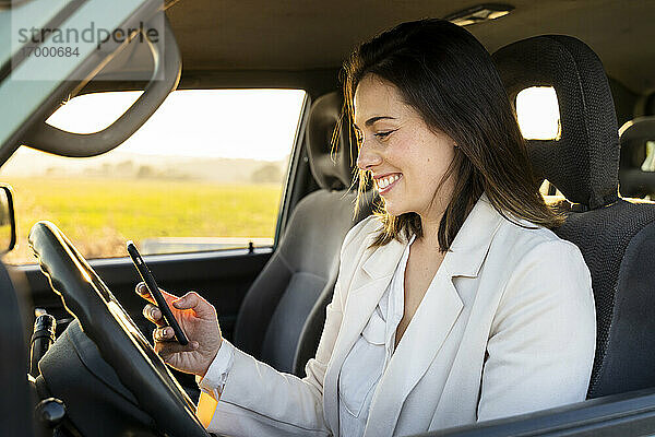 Glückliche junge Frau  die während einer Autoreise ihr Smartphone im Auto benutzt