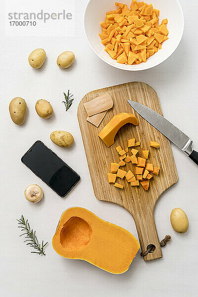 Studioaufnahme von Smartphone  rohen Kartoffeln und Schneidebrett mit geschnittenem Kürbis