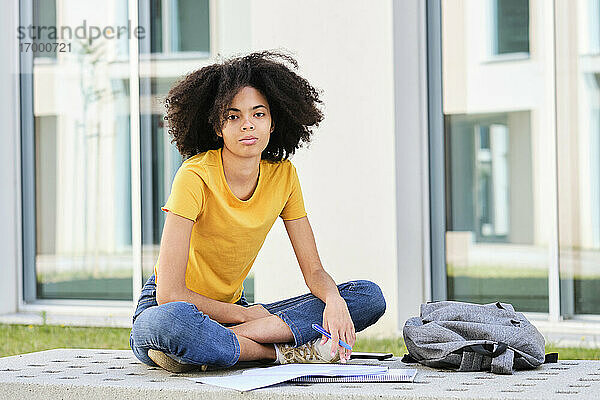 Student mit Buch  der auf dem Universitätscampus sitzt und studiert