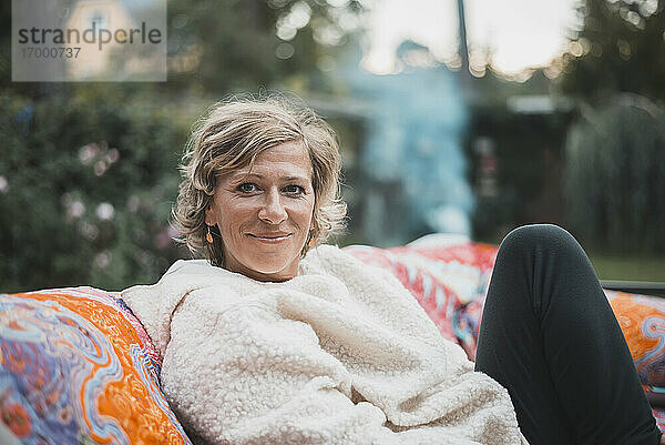 Lächelnde Frau  die sich auf dem Sofa im Hinterhof entspannt