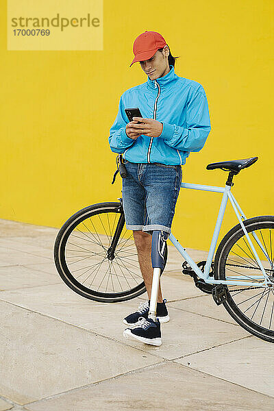 Mann telefoniert  während er mit dem Fahrrad an einer gelben Wand steht