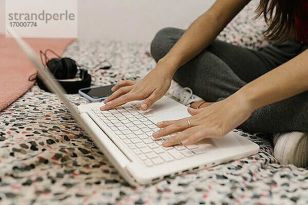 Teenager-Mädchen probiert einen Laptop aus  während sie auf dem Bett sitzt