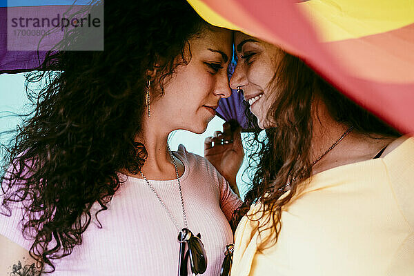 Nahaufnahme eines lesbischen Paares mit Regenbogenfahne  das sich im Freien vergnügt