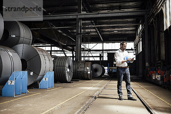 Männlicher Unternehmer  der mit seinem Smartphone Nachrichten schreibt  während er in einer Fabrik steht