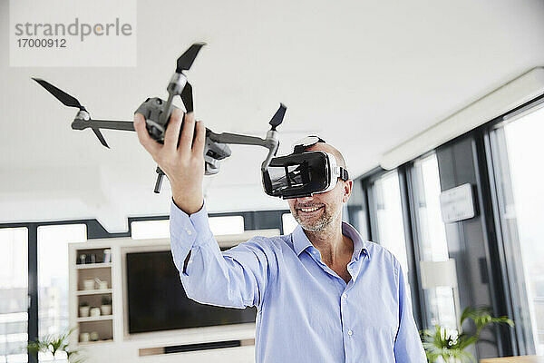 Unternehmer trägt ein Virtual-Reality-Headset und hält einen Quadcopter  während er zu Hause steht