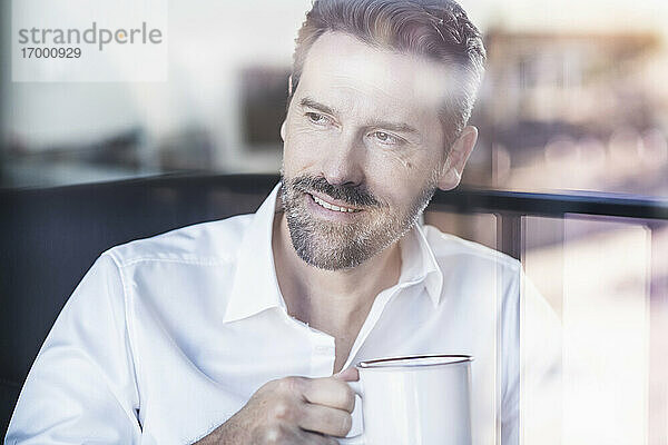 Lächelnder Geschäftsmann  der im Büro sitzend Kaffee trinkt