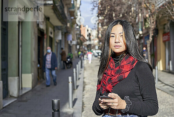 Schöne junge Frau  die ein Mobiltelefon benutzt  während sie auf der Straße in der Stadt steht