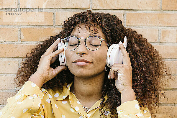 Frau mit geschlossenen Augen hört Musik und lehnt sich an die Wand