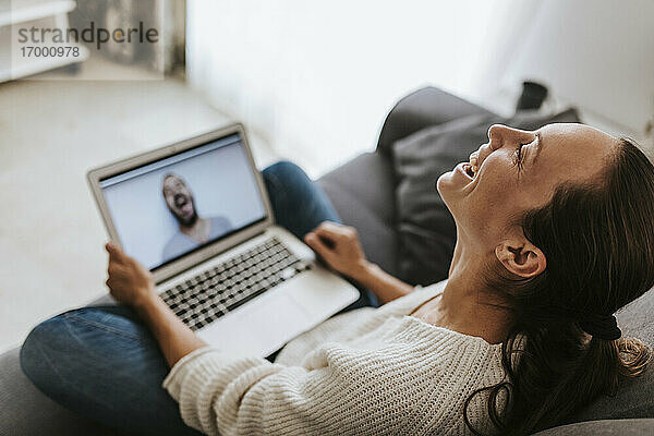 Frau lacht während eines Videoanrufs mit einem männlichen Freund zu Hause