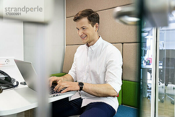 Junger Geschäftsmann mit Laptop im Büro sitzend