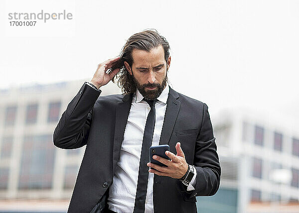 Porträt eines bärtigen Geschäftsmannes  der im Freien steht und ein Smartphone in der Hand hält