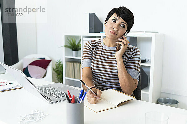 Porträt einer Geschäftsfrau  die am Schreibtisch mit einem Smartphone telefoniert