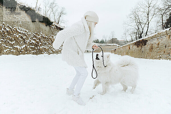 Junge Frau spielt mit ihrem Hund im Schnee