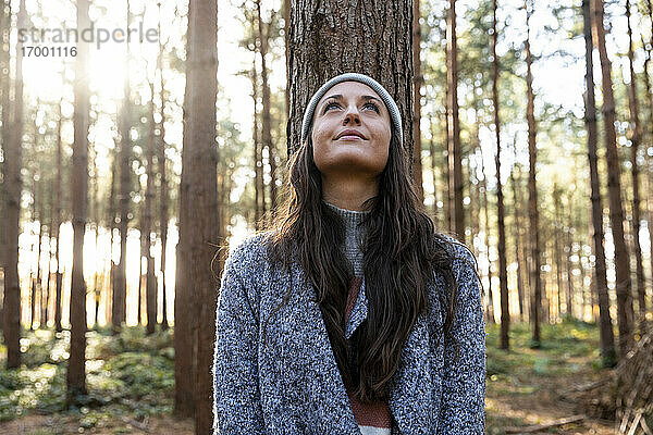 Nachdenkliche Frau  die nach oben schaut  während sie an einem Baumstamm im Wald von Cannock Chase steht