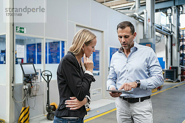 Geschäftsmann erklärt einer Kollegin in einer Fabrik das digitale Tablet.