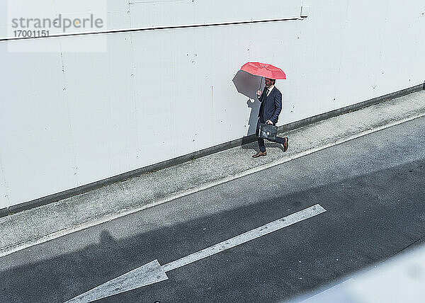 Geschäftsmann mit Regenschirm  der auf einer Straße mit einem Pfeilschild geht