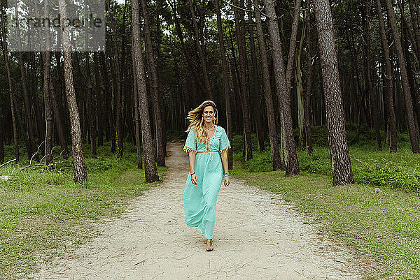 Mittlere erwachsene Frau lächelt beim Spaziergang auf einem Waldweg