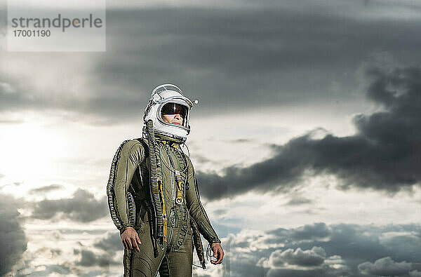 Mann posiert als Astronaut gekleidet mit dramatischen Wolken im Hintergrund