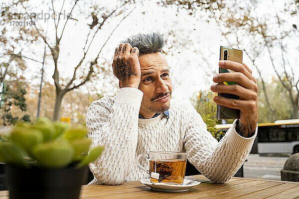 Müder Mann  der in einem Café sitzt und sein Smartphone benutzt