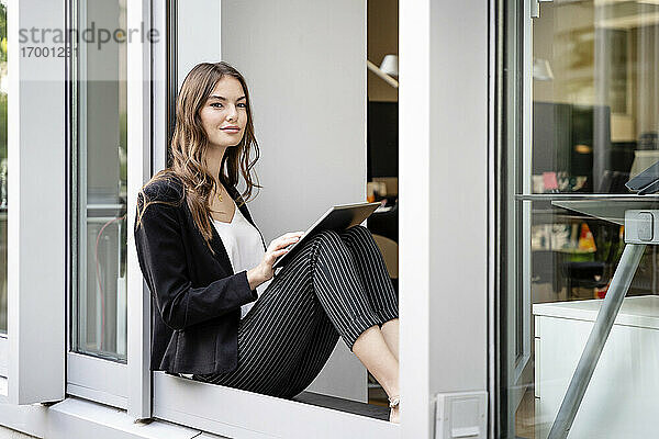 Junge Geschäftsfrau  die ein digitales Tablet benutzt  während sie an der Bürotür sitzt