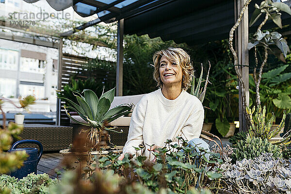 Lächelnde Frau  die inmitten von Pflanzen auf einem Dachgarten wegschaut
