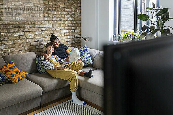 Lächelndes lesbisches Paar  das zu Hause auf dem Sofa sitzt und fernsieht