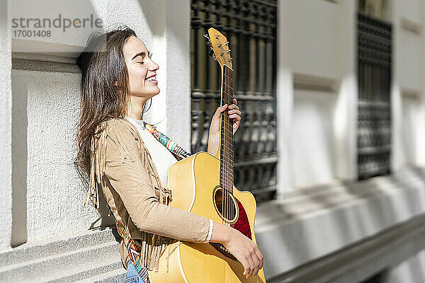 Lächelnde Musikerin spielt Gitarre in der Stadt an einem sonnigen Tag
