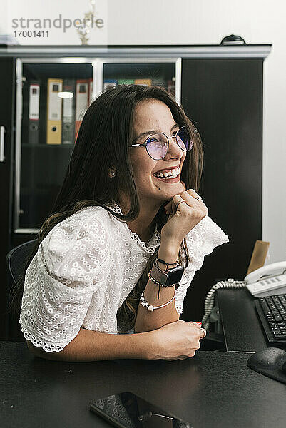 Geschäftsfrau lächelt  während sie mit der Hand am Kinn im Büro sitzt