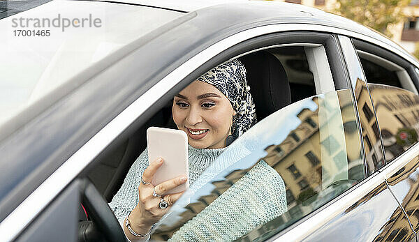 Frau mit Kopftuch  die ein Mobiltelefon benutzt  während sie in einem Auto in der Stadt sitzt