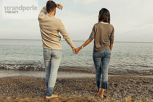 Junges Paar schaut auf das Meer und steht auf Sand