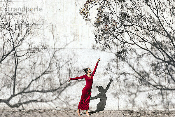 Frau in rotem Kleid mit Tänzerin Pose und Baum Schatten an der Wand