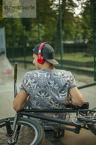 Junger Mann hört Musik  während er sich auf einem BMX-Fahrrad in einem Skateboard-Park entspannt