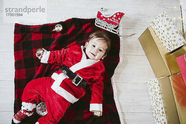 Lächelnder kleiner Junge im Weihnachtsmannkostüm  der zu Hause auf einer Decke liegt  während Weihnachten