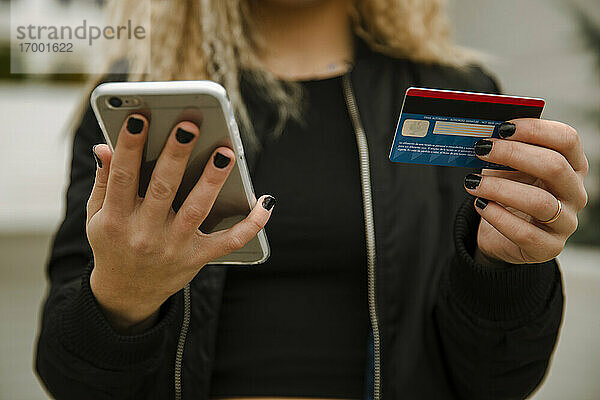 Junge Frau beim Einkaufen mit Smartphone und Kreditkarte