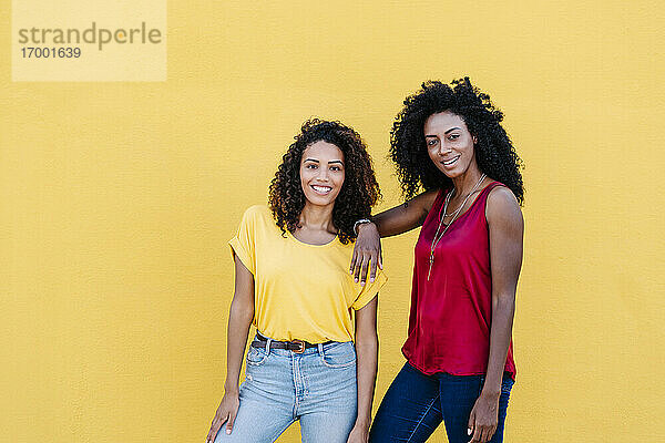 Lächelndes lesbisches Paar mit cooler Einstellung gegen gelbe Wand