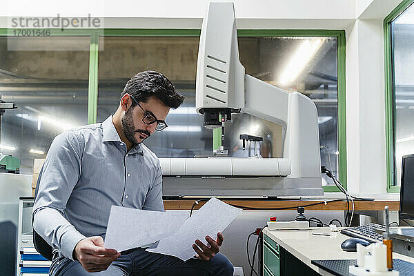 Männlicher Unternehmer liest ein Dokument  während er in der Industrie sitzt