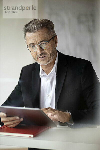Geschäftsmann mit Brille  der bei der Arbeit zu Hause ein digitales Tablet benutzt