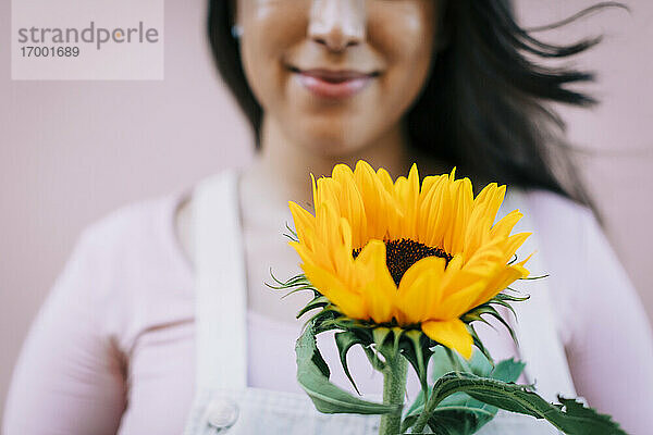 Junge Frau vor rosa Wand  hält Sonnenblume