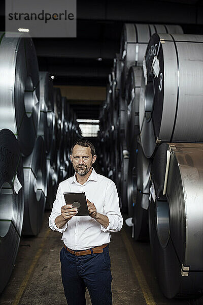 Männlicher Unternehmer  der ein digitales Tablet hält  während er in der Fertigungsindustrie steht