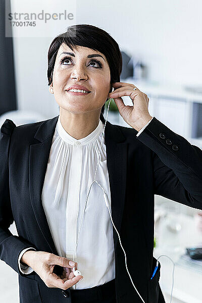 Porträt einer lächelnden Geschäftsfrau  die ein Smartphone mit Kopfhörern benutzt