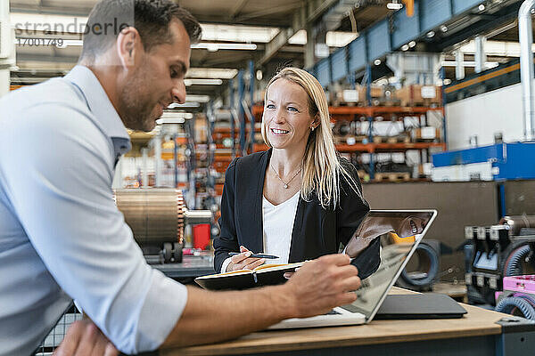 Lächelnder weiblicher Kollege  der einen männlichen Unternehmer ansieht  während er in einer Fabrik steht