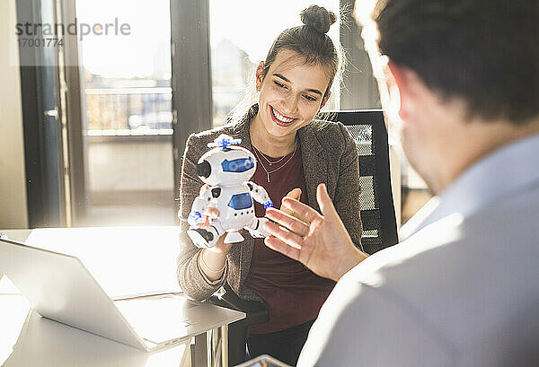 Junge Geschäftsfrau zeigt einem Geschäftsmann ein Roboterspielzeug  während sie im Büro sitzt