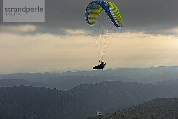 Luftaufnahme eines männlichen Gleitschirmfliegers  der in der Abenddämmerung über den Bergen schwebt