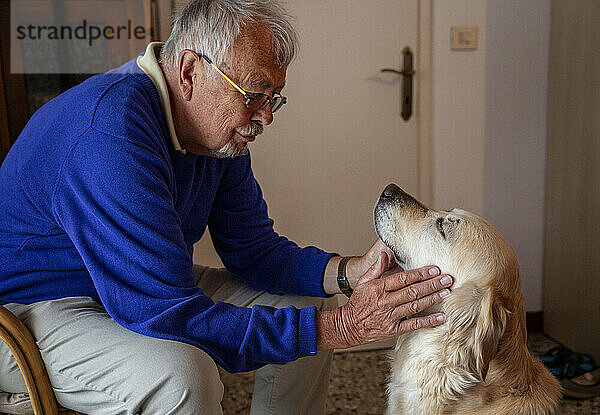 Älterer Mann mit Hund sitzt zu Hause