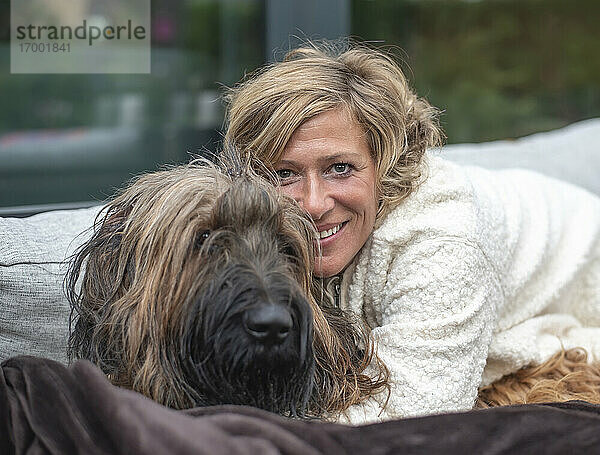 Lächelnde Frau  die ihren Hund umarmt  während sie auf dem Sofa im Hinterhof sitzt