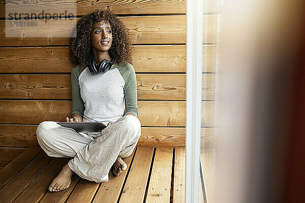 Frau mit digitalem Tablet  die zu Hause im Schneidersitz sitzt